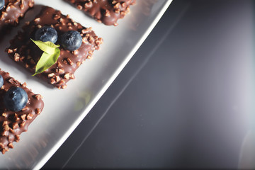 Chocolate dessert with nuts and fresh berries. Sweet snack for coffee biscuit in glaze and nut crumbs with fruit.