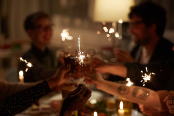 Group of young people sitting at the table and holding sparklers and having fun during party