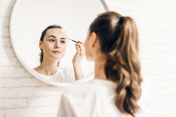 Portrait of beautiful smiling woman looking in mirror and applying mascara.	