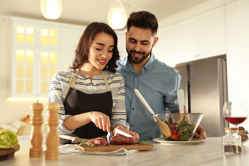 Lovely young couple cooking meat together in kitchen