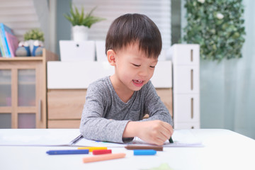Cute happy smiling Asian 3 - 4 years old toddler boy child coloring with crayons at home, Creative play for toddler, improve focus in child concept