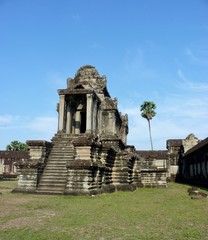Naklejka premium Stone library building of Angkor Wat on green grass before blue sky, ruins of Angkor, Cambodia
