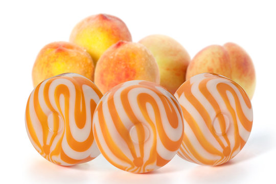 Three round milk caramel with peach flavor and four peaches on a white background