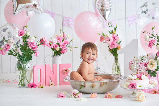 Smash cake party. Little cheerful birthday girl with first cake. Happy infant baby celebrating his first birthday. Decoration and photo zone for first year. One year baby celebration. Pink decor.