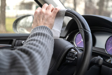Man cleaning steering wheel of a car using antivirus antibacterial wet wipe (napkin) for protect...