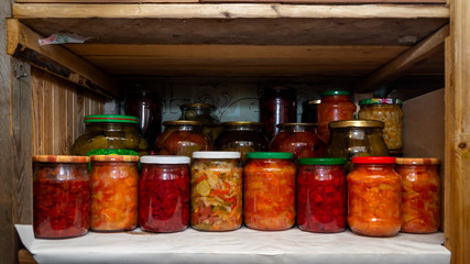 Wooden shelf in pantry with provisions in glass jars with pickled vegetables