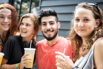 People from different ethnic groups smiling with a juice in a plastic container in their hands and with bracelets with the lgtb flag