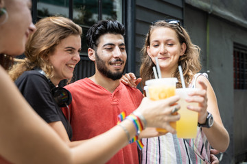 Group of four young people of different ethnicities toasting with juice in a plastic cup