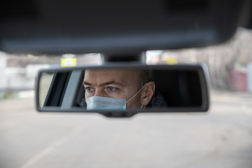 Reflection of face of middle aged man in the medical mask for protect himself from bacteria and virus while driving a car in the car rear view mirror. Coronavirus. Pandemic