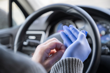 Man puts on rubber gloves for protect himself from bacteria and virus while driving a car. Coronavirus. Pandemic