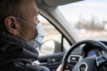 face of middle aged man in the medical mask for protect himself from bacteria and virus driving a car. Coronavirus. Pandemic