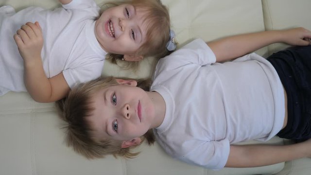 happy family kids brother and sister play on the couch laugh tickle each other. children little boy and girl play indoors laughing and fun happy childhood lifestyle