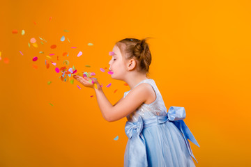 happy little girl in a blue dress holds a gift bag and catches confetti while standing on a yellow...