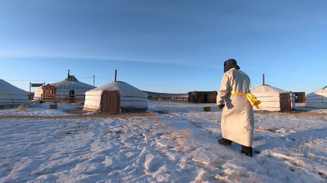 Adult Man Wearing Traditional Nomadic Mongolian Deel Walks Past Ger.