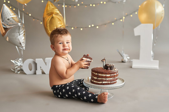Smash cake party. Little cheerful birthday boy with first cake. Happy infant baby celebrating his first birthday. Decoration and photo zone for first year. One year baby celebration. Grey decor.