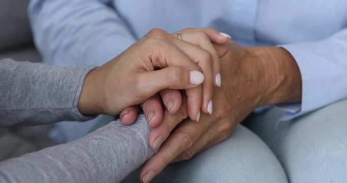 Close up young female woman holding hands of retired older grandmother, helping solving problems. Kind empathic grown up daughter supporting comforting middle aged mother, trustful relations concept.