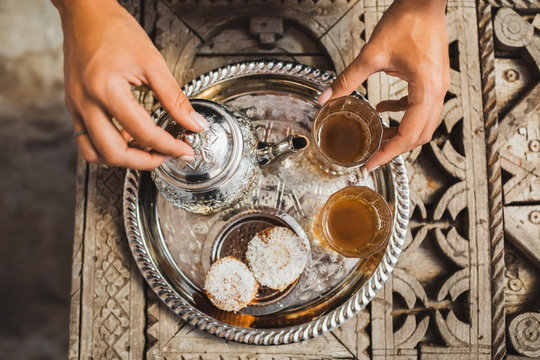 Woman hands serving traditional moroccan mint tea ceremony with cookies and vintage silver teapot. Hospitality and service in Morocco, Marrakech.