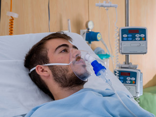 Teenage boy with a beard and wearing an oxygen mask, in a hospital room