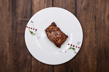 Juicy Striploin Steak: thin edge of the beef, thyme and olive oil in a plate on a wooden table.