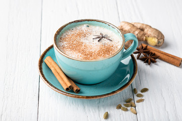 Masala tea in a ceramic cup with cardamom, star anise, cinnamon and ginger on a wooden background. Antiviral drink for immunity. Top view, place for text.