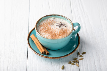 Masala tea in a ceramic cup with cardamom, star anise, cinnamon and ginger on a wooden background. Antiviral drink for immunity. Top view, place for text.