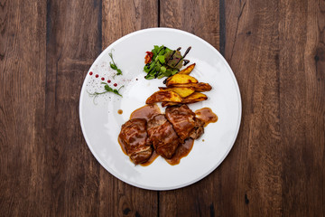 Saltimbocca. Beef chop with Parma ham and baked potatoes. Beef fillet, Parma ham, sage, mixed salad and sun-dried tomatoes in a plate on a wooden table. Italian cuisine.