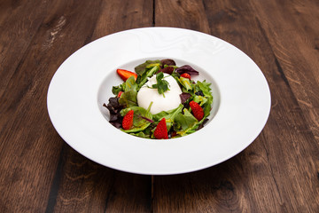 Fresh Italian buratta cheese with mixed salad leaves and strawberry in a plate on a wooden table. Italian cuisine.