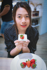 A girl eating an strawberry in a pastry shop