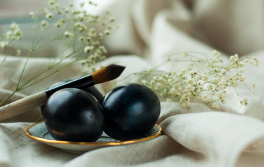 black eggs on a plate with a gold border and a brush on a gray linen background