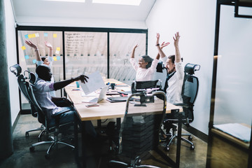 Multiethnic excited colleagues rejoicing in success during meeting in office
