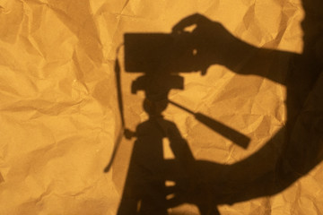 Shadow of photo camera on tripod and woman hand pressing the shoot button. Yellow crumpled paper as background.