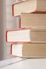 Stack of books at window. 4 heavy books with red covers.
