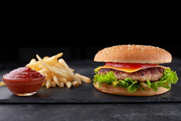 Cheeseburger with meat, potatoes and sauce, on a black background