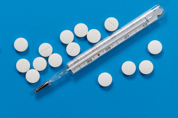 Medical mercury thermometer showing high body temperature and lots of round white pills on blue...
