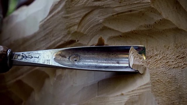 Close up of a craftsman who carves a wooden sculpture with hammer and chisel