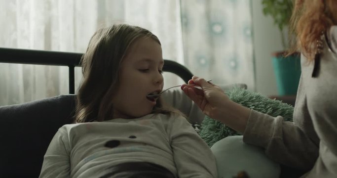Mama podaje chorej c&oacute;rce lekarstwo.