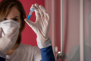 nurse wearing white surgical gloves and holding molded mask while examining a test tube with coronavirus flu vaccine in the medical laboratory to study a cure to stop the pandemic in the world