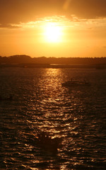 Naklejka premium Silhueta de barcos atravessando rio com ondas em contraluz durante o pôr-do-sol