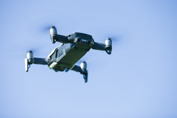 Fototapeta na wymiar Four-propeller drone flying in nature against the blue sky. The maneuver.