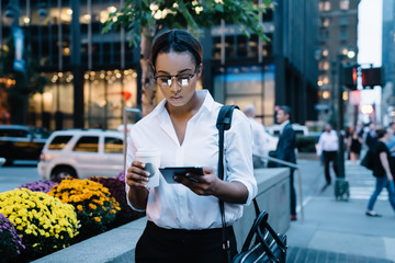 Black woman with takeaway beverage using tablet on street