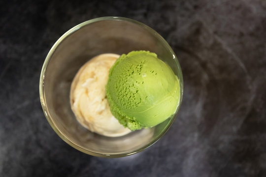 Green tea matcha and salt caramel ice cream scoop in glass on a grey stone background. Top view and copy space.