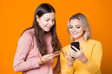 Blonde and brunette with their smartphones on a bright yellow background.