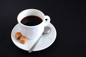 Set: a mug, a teaspoon, a saucer and two pieces of sugar. On black background.