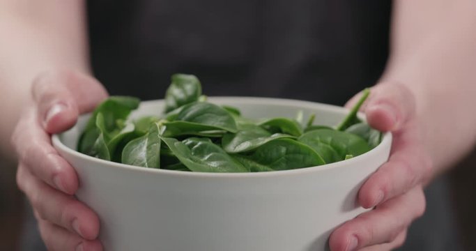 Slow motion man show fresh spinach leaves in white bowl closeup