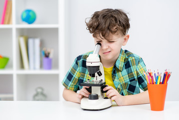 Young boy doing a homework and uses the microscope at home