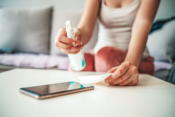 Woman's hands wipe smartphone screen with disinfectant spray. Close-up woman cleans her mobile phone at home. Close up view of woman hand cleaning smartphone screen with alcohol