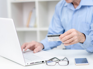 Senior man holds credit card and uses laptop. Online shopping