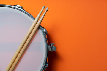 Drum stick and drum on orange table background, top view, music concept