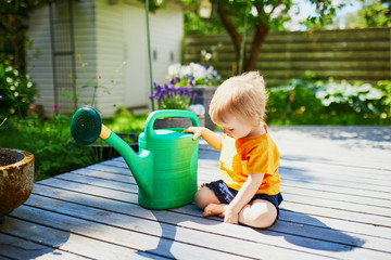 Cute baby girl playing with watering pot a warm summer day © Ekaterina Pokrovsky
