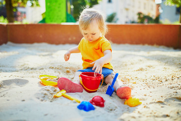 Adorable little girl having fun on playground in sandpit